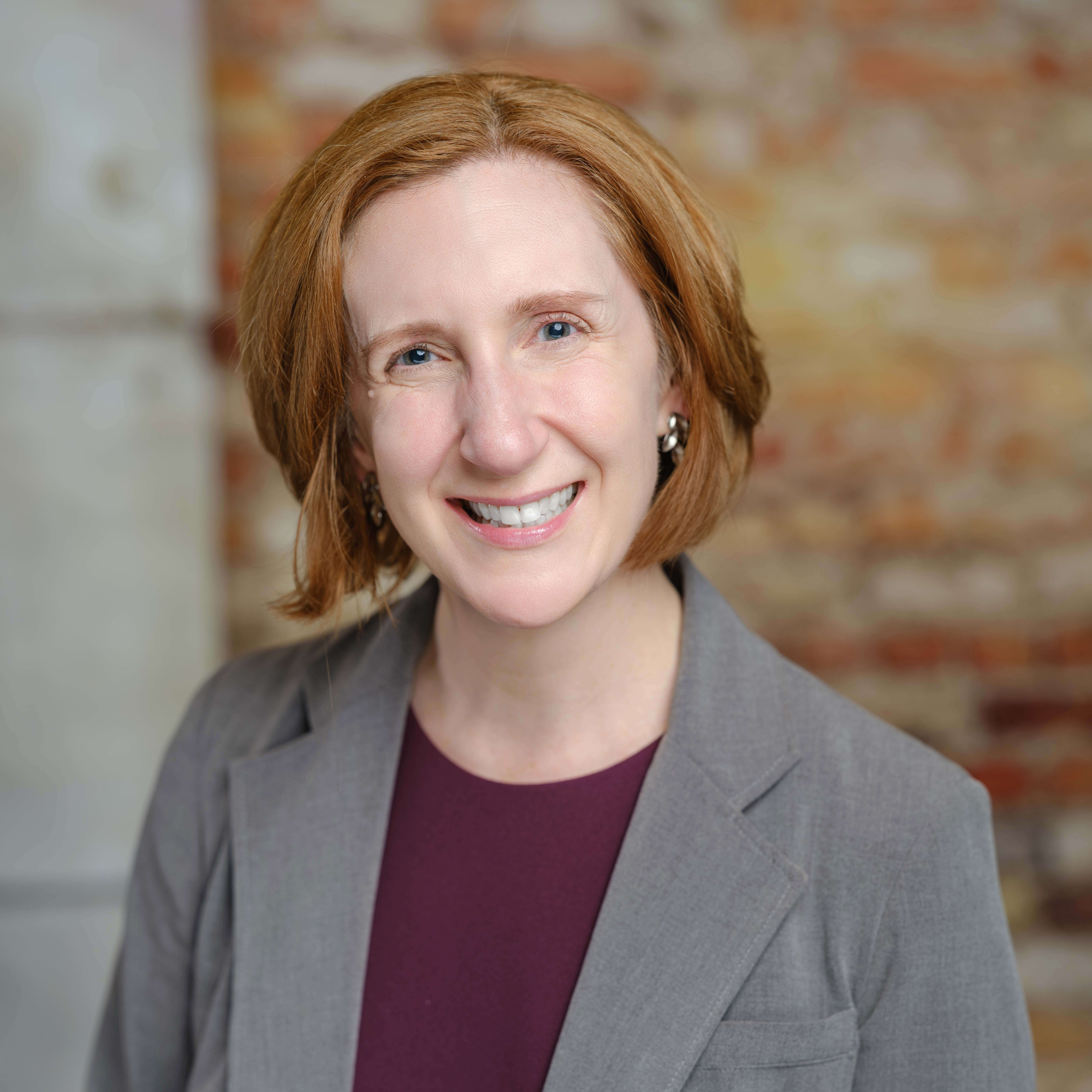 headshot of a woman in a tan suit with maroon shirt