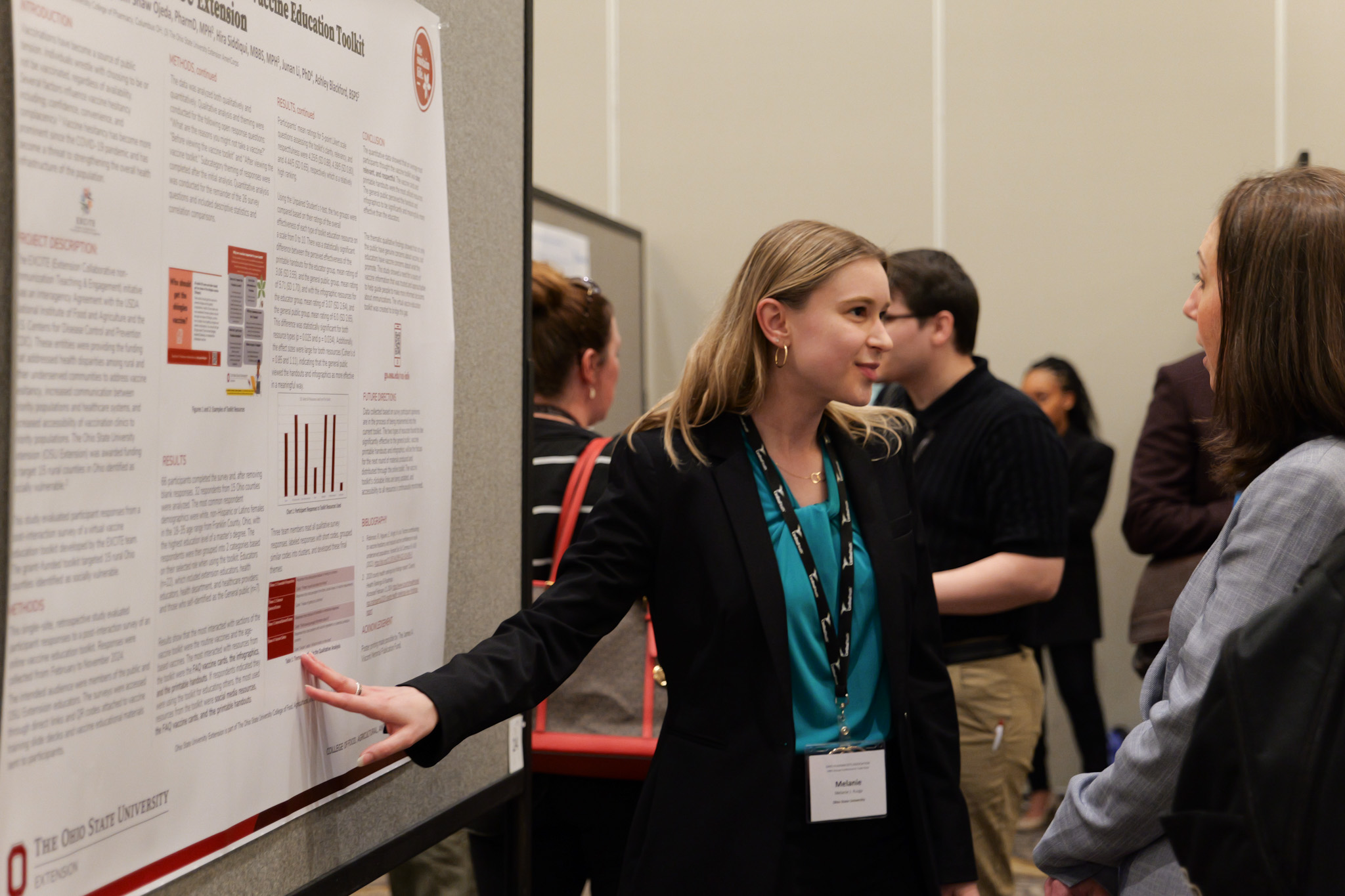 Ruzga standing in front of her research poster at the OPA poster session, speaking to a viewer