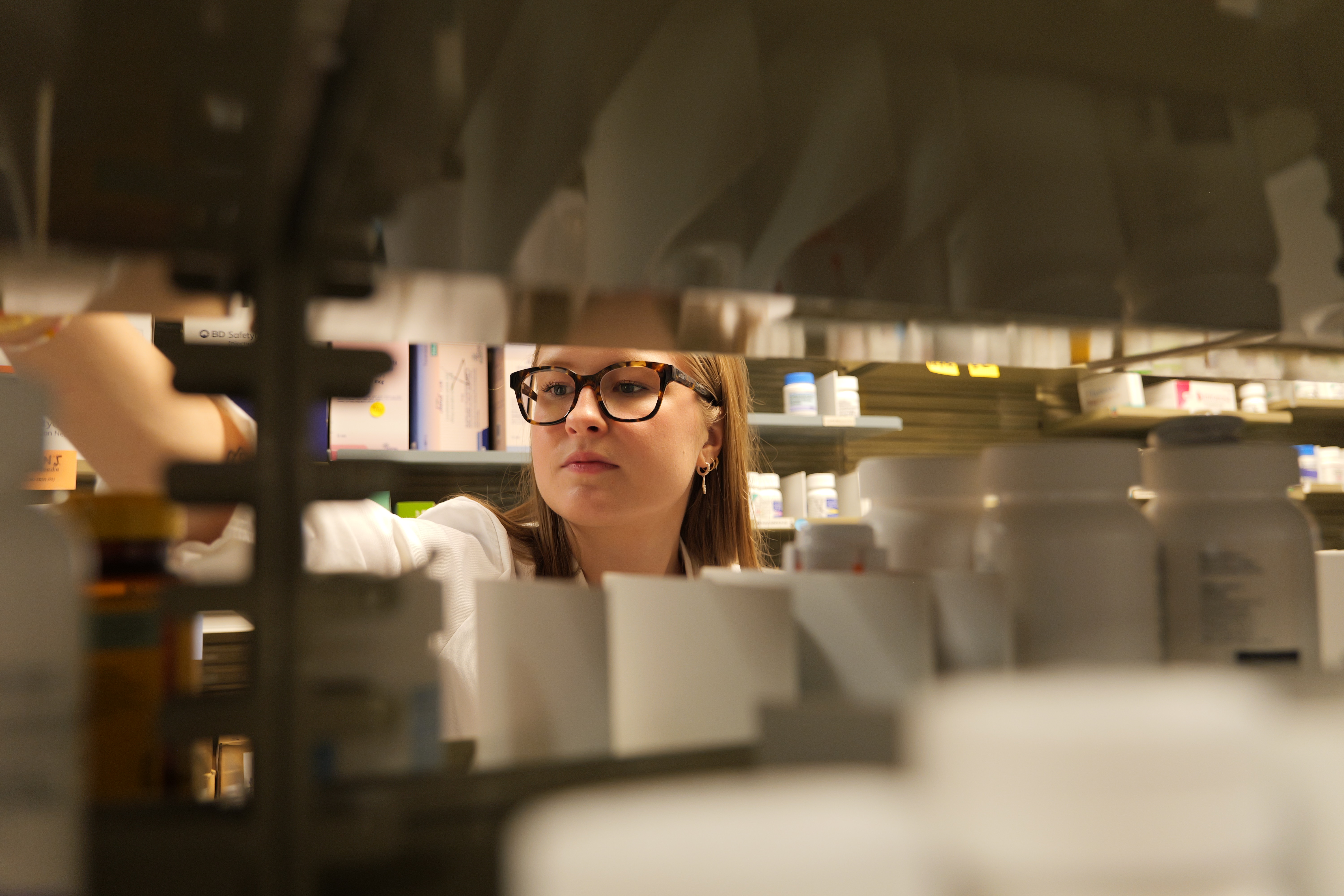 Pharmacist reaching to grab medicine  on pharmacy shelf