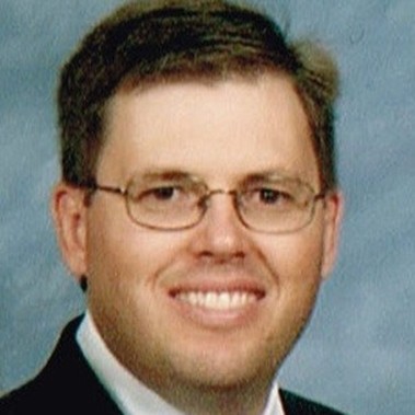 headshot of a person in a suit with glasses