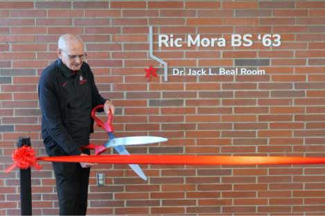 Ric Mora holding large red scissors about to cut the red ribbon, officially unveiling the Dr. Jack L. Beal Room.