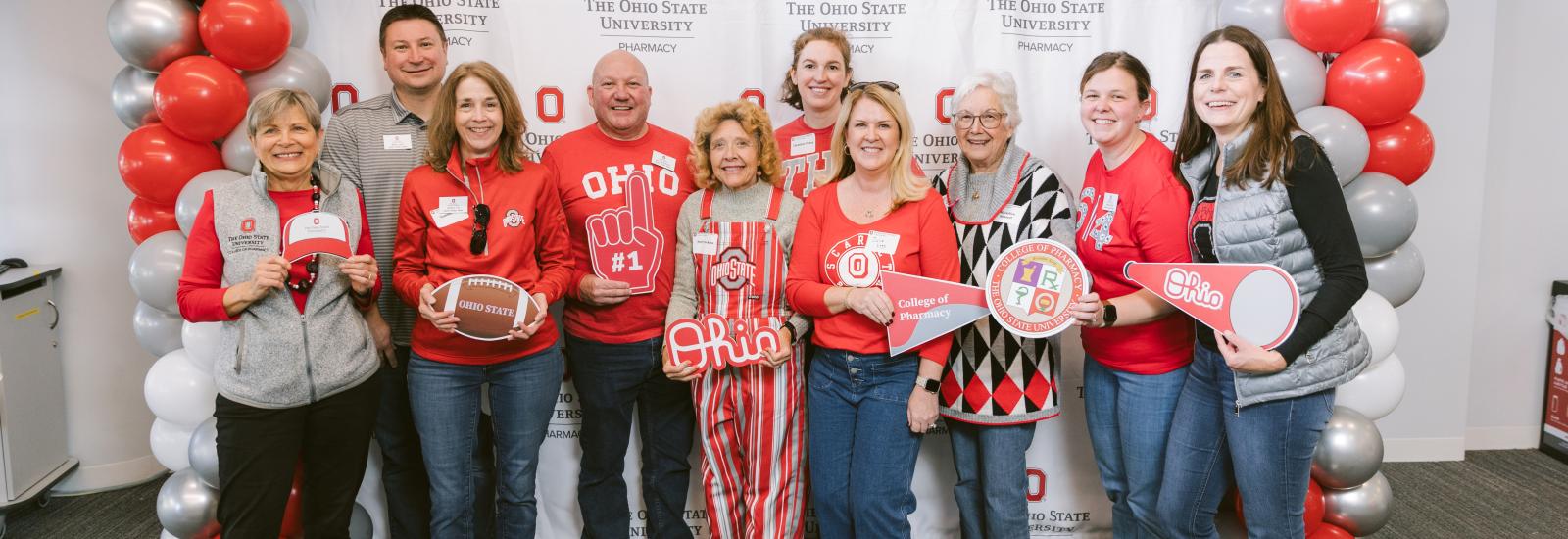 alumni in buckeye gear posing in front of college media wall