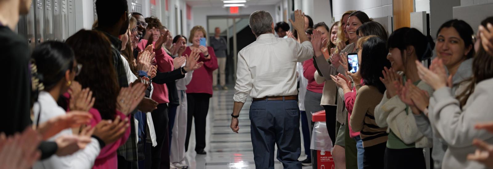 Dr. McAuley walking down a hallway to students applauding