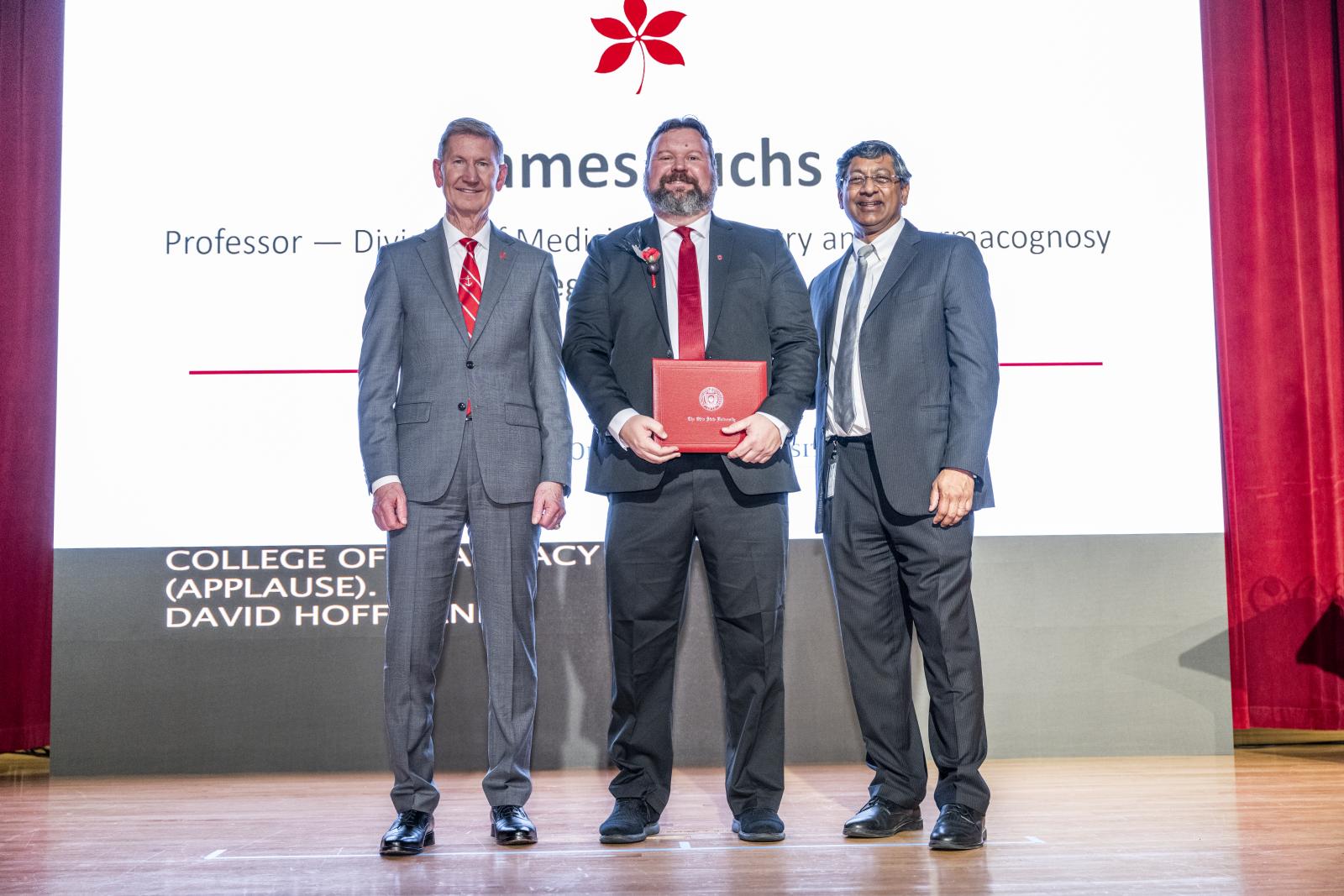 jim fuchs receiving award on stage with president and provost