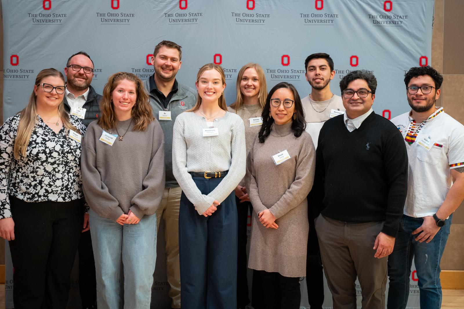 a group of students and alumni posing in front of a media wall with OSU logos