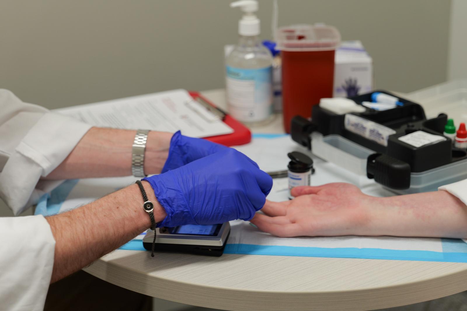 Gloved hands administering a blood glucose test via needle stick