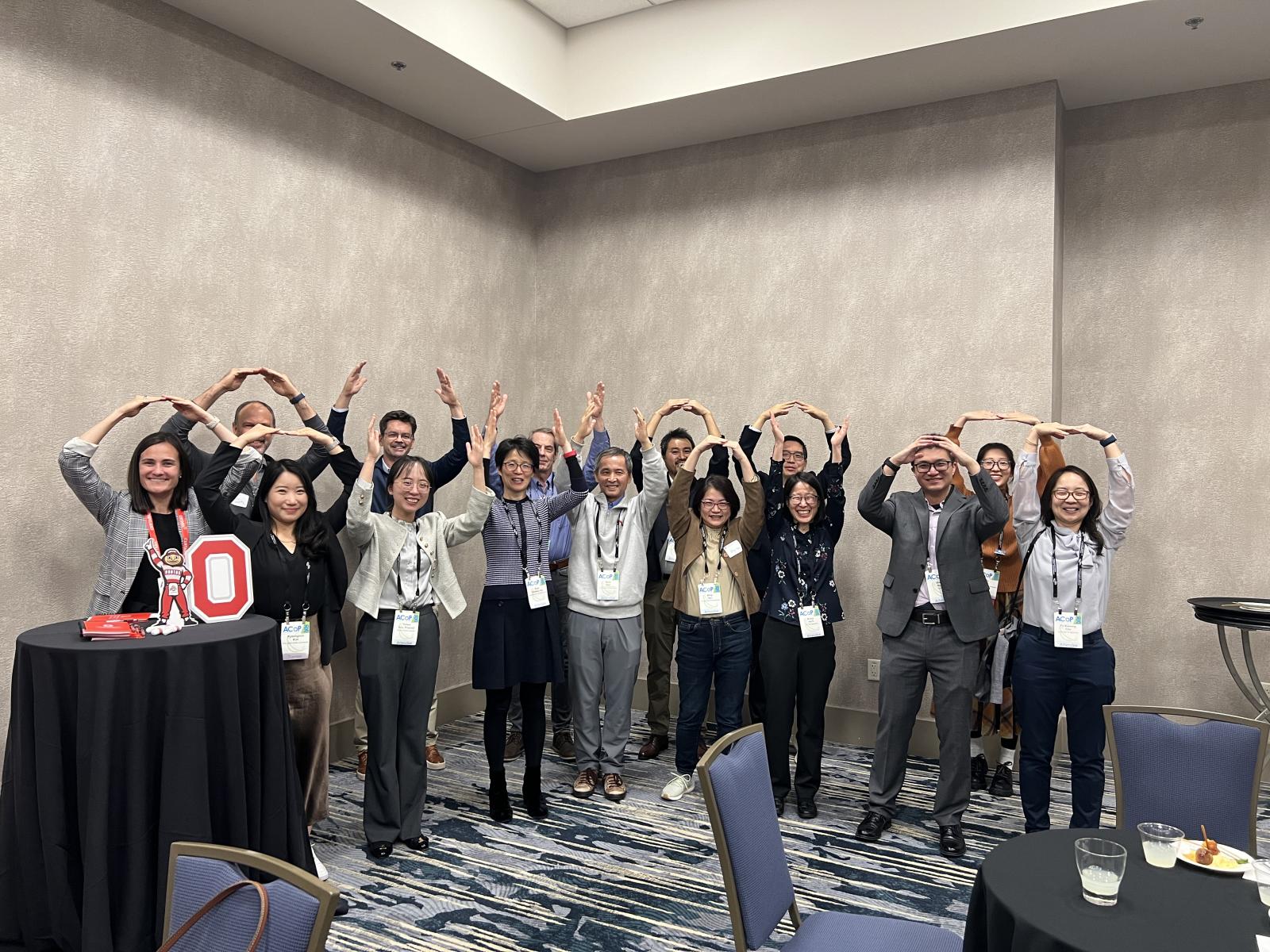 A group photo of the graduate program alumni's making the letter "O" with their arms in the air. 