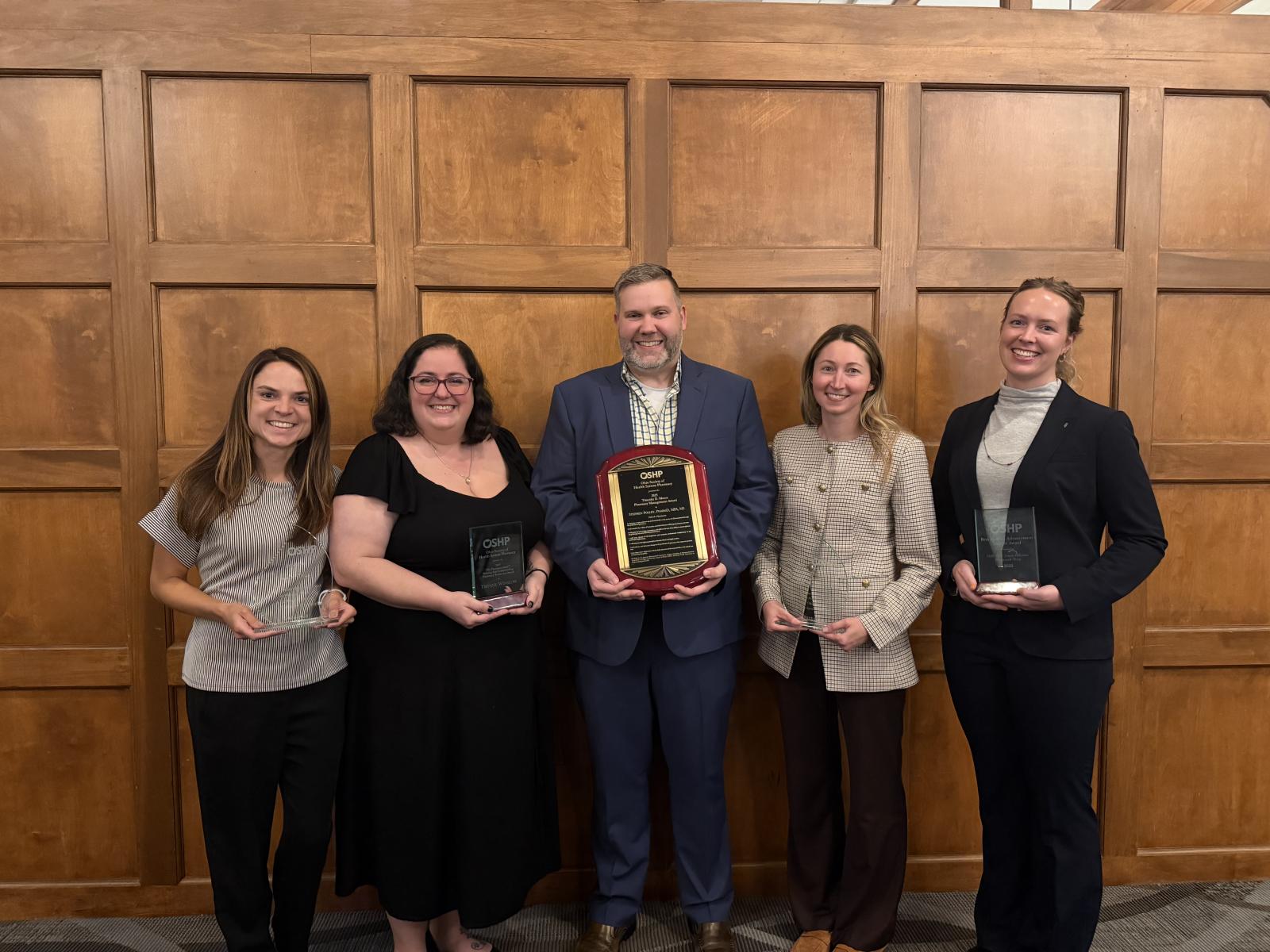 A group of five people holding award plaques