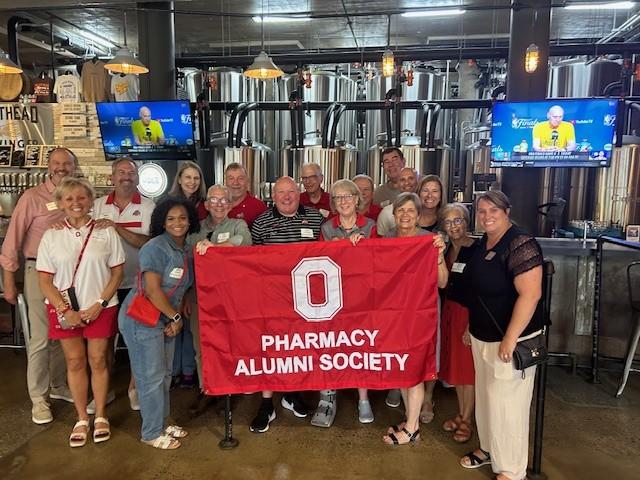 a large group holding a pharmacy alumni society flag