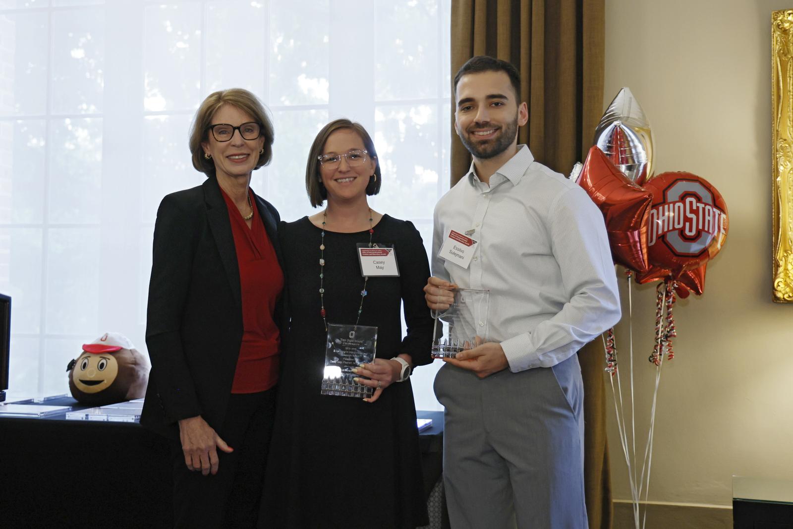 Three individuals standing, two holding awards