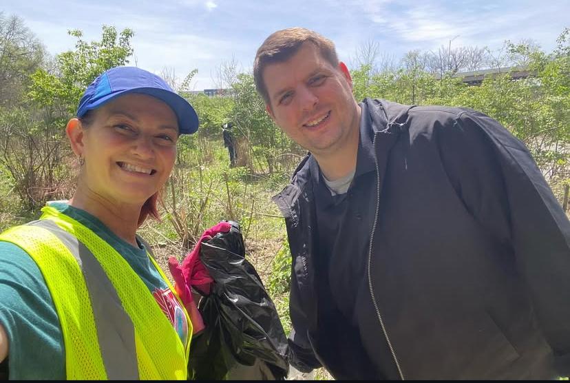 two people pose for a photo outside holding a trash bag