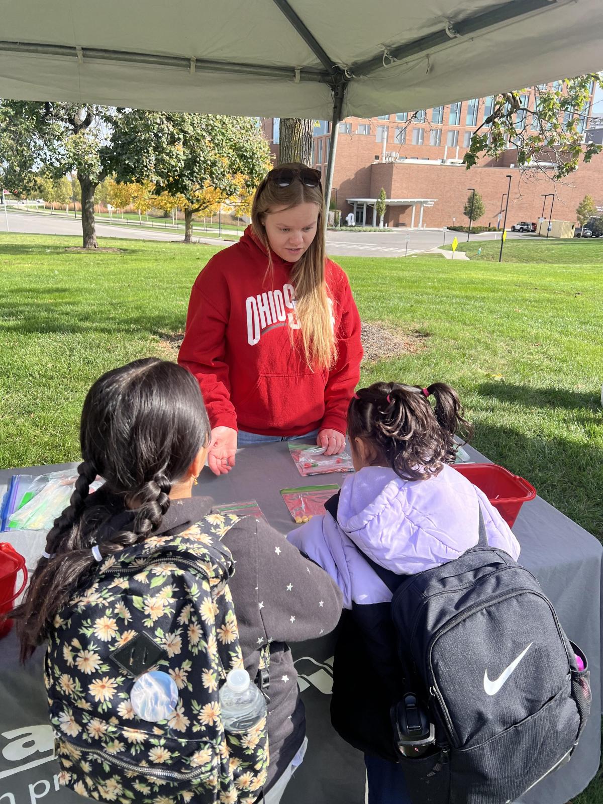 Two girls talking to a woman at the table. 