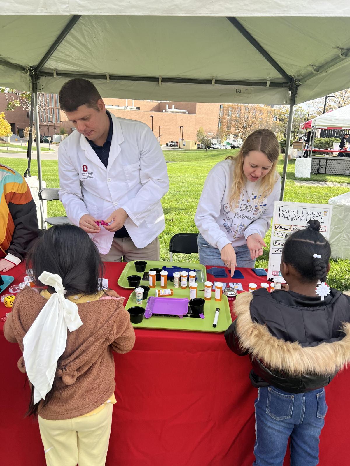 Two girls observing a man and woman discuss pharmacy topics. 