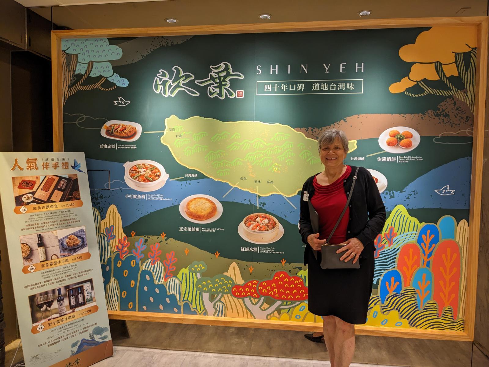 woman posing in front of large painting and menu