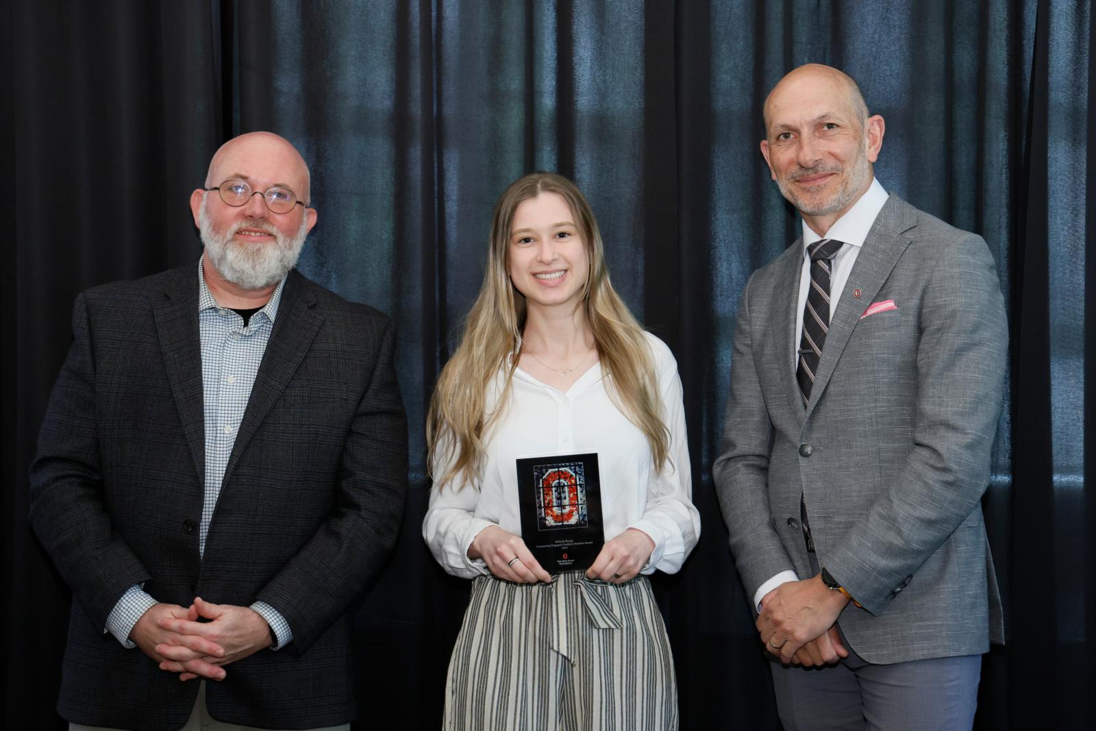 a person holding a plaque with two people around them posing
