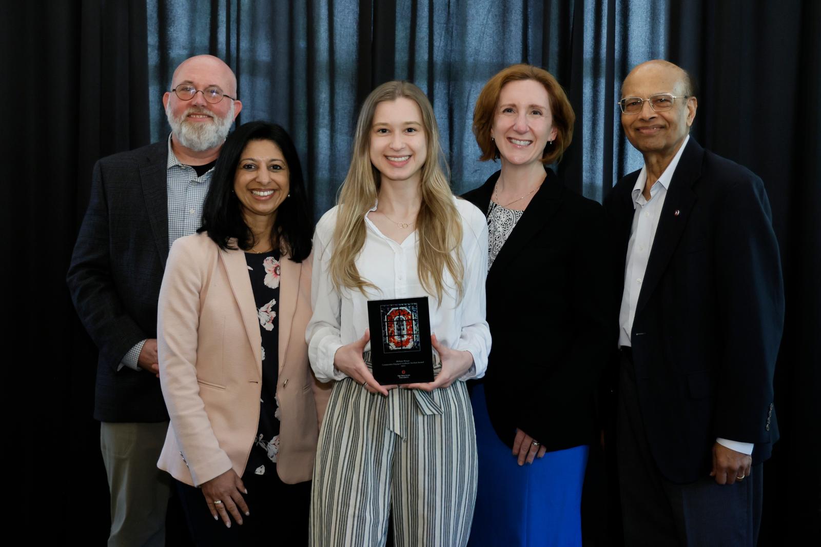 five people posing with the center person holding a plaque