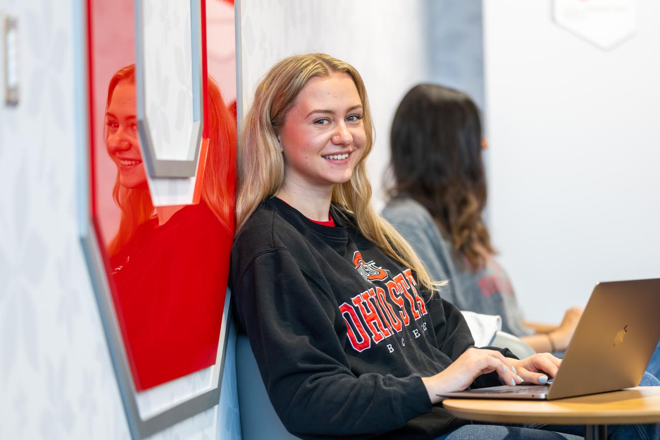 a student with a laptop sitting and leaning against a wall