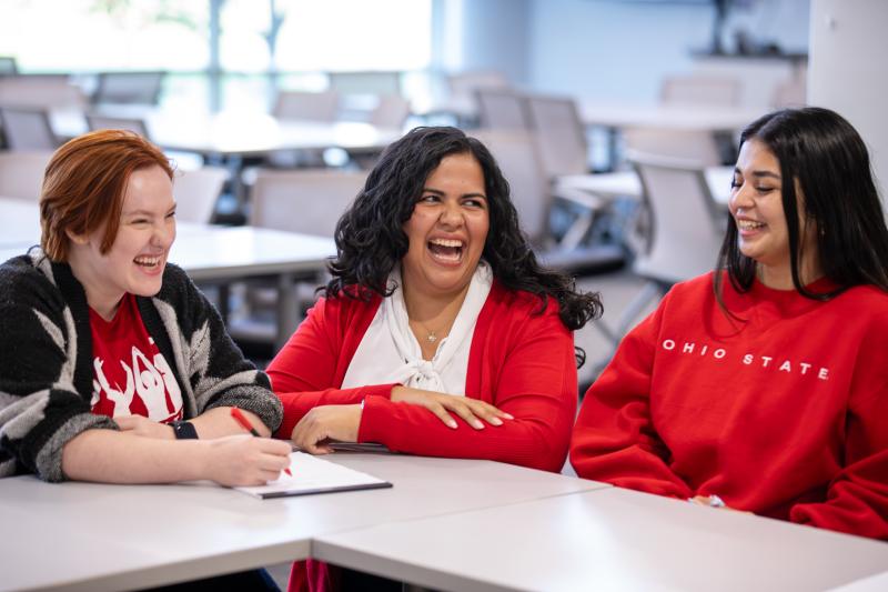 an instructor kneeling at a table laughing with students