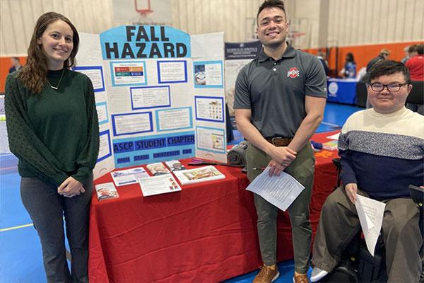 three students pose next to table exhibit about fall hazard