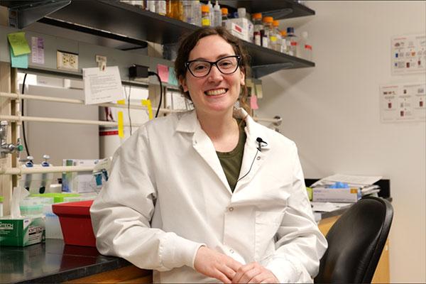 a researcher posing for camera in white coat in research lab