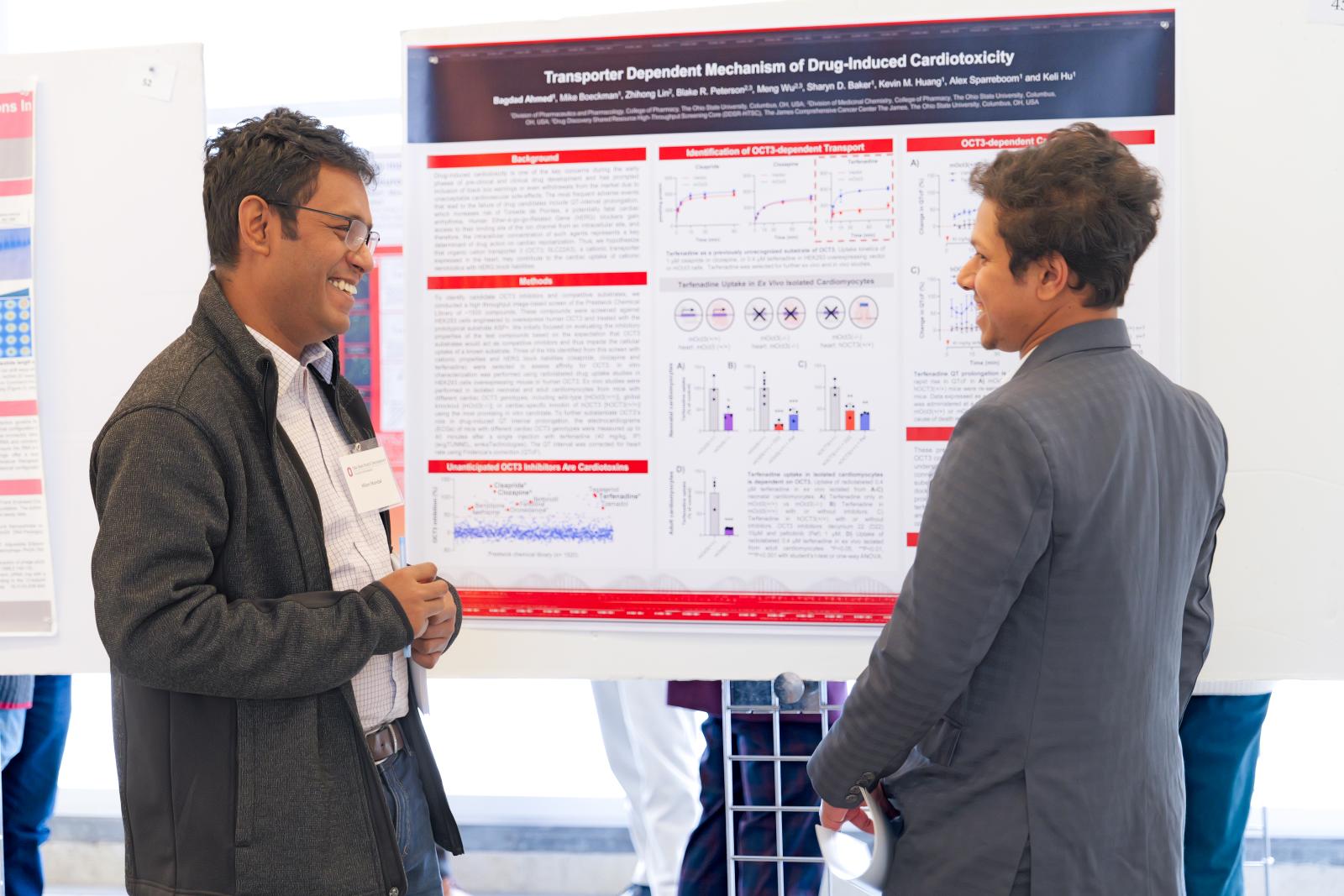 Fellow Milon Mondal speaking with another college member in front of research poster