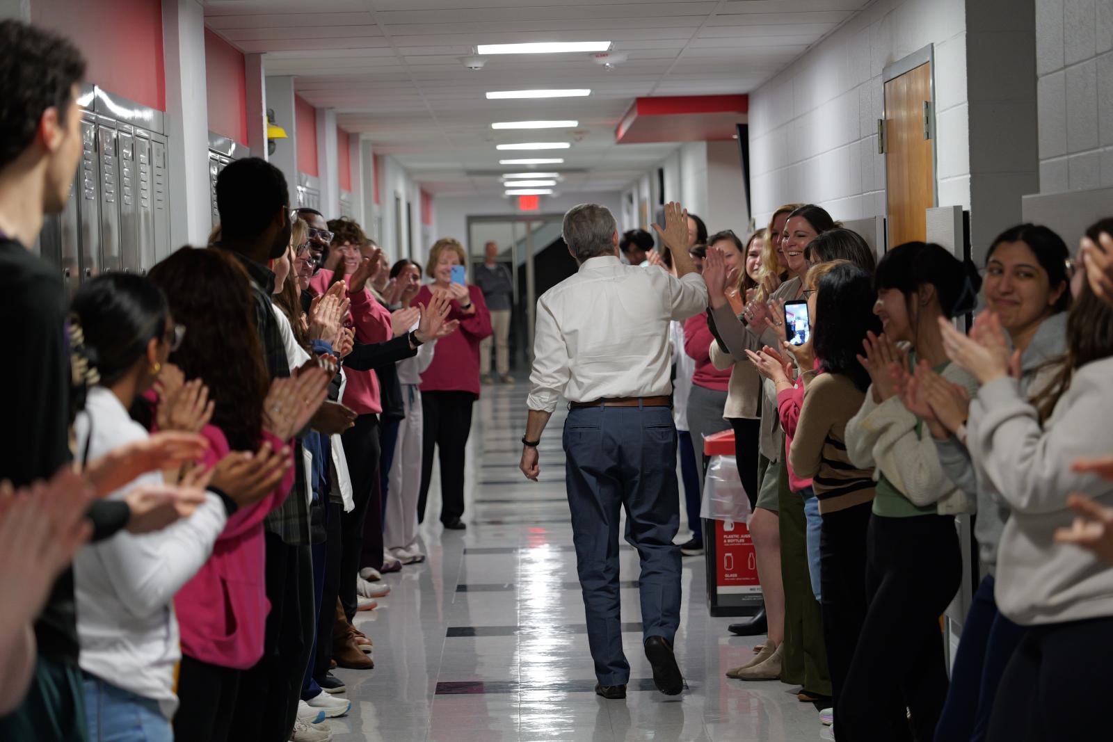 Dr. McAuley walking down a hallway to students applauding